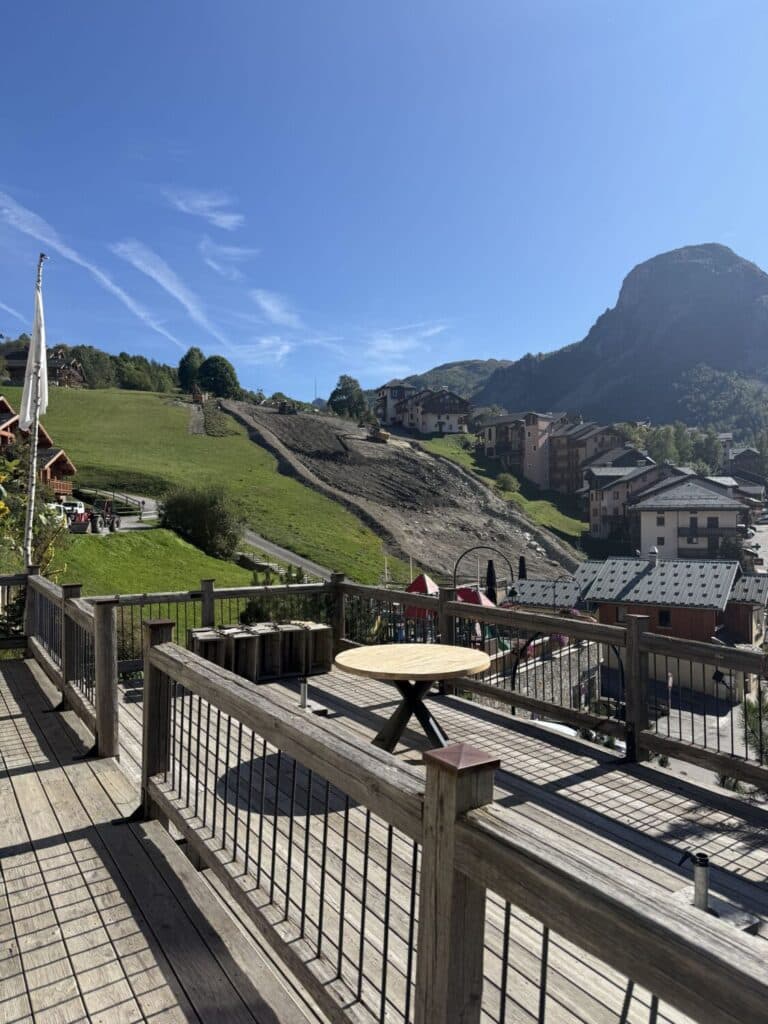 Terrasse en bois du restaurant Le Montagnard en été avec vue panoramique sur la vallée et les montagnes de Saint-Martin-de-Belleville